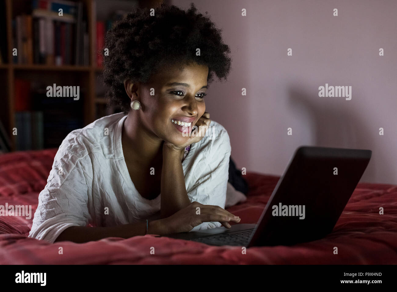 Portrait of smiling young woman lying on her bed using laptop Stock ...
