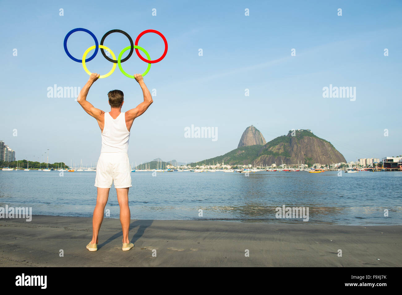 RIO DE JANEIRO, BRAZIL - NOVEMBER 10, 2015: Athlete holds Olympic rings on the shore of Botafogo Beach near Sugarloaf Mountain. Stock Photo