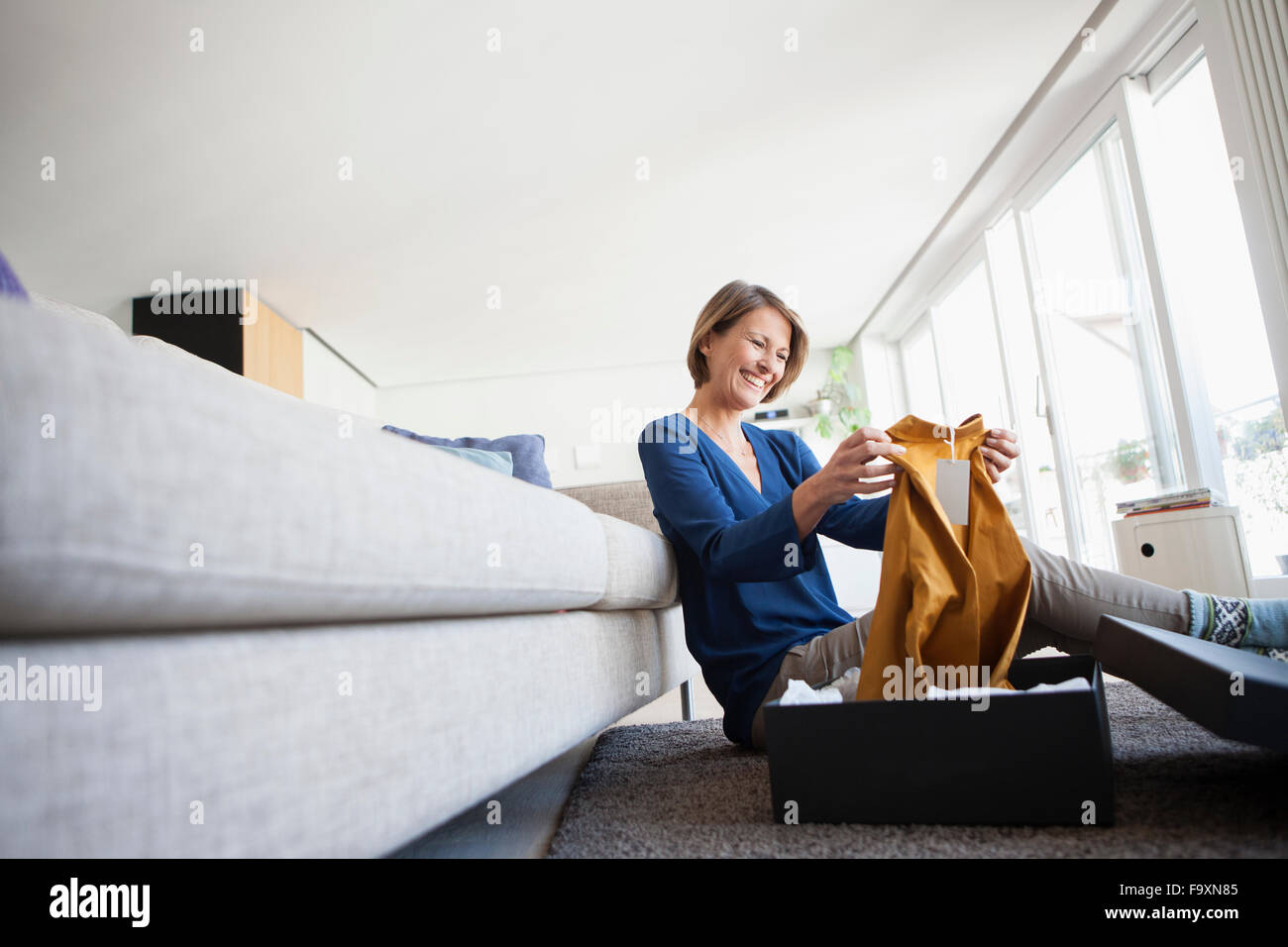 Smiling woman at home unpacking parcel with garment Stock Photo