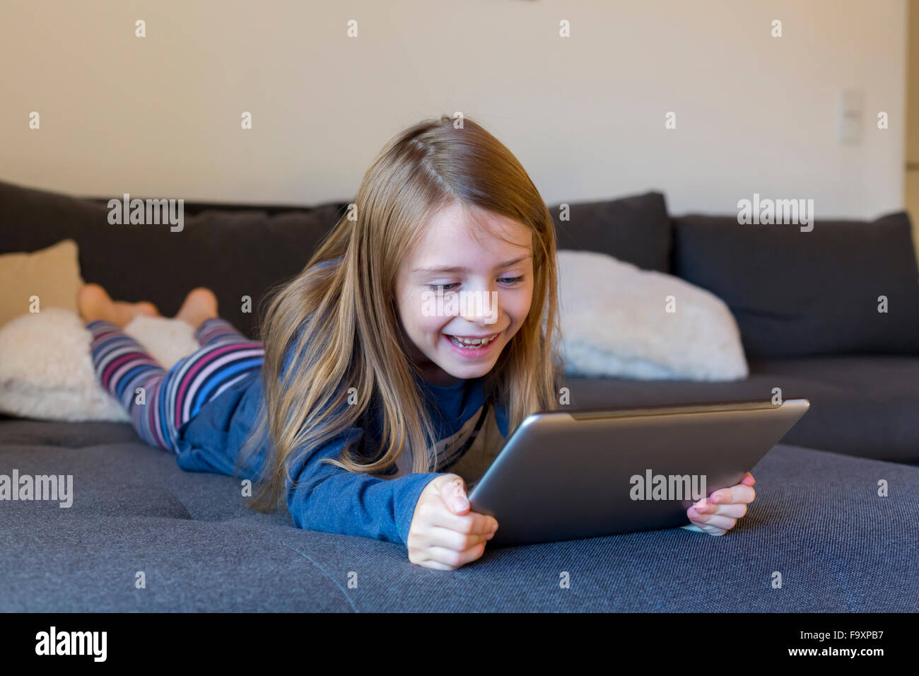 Smiling girl lying on the couch using digital tablet Stock Photo - Alamy