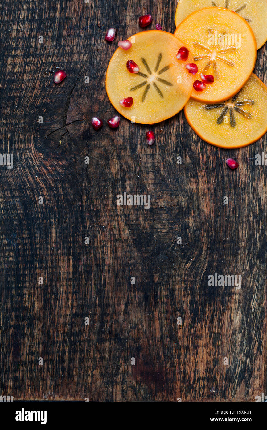 Kaki slices and pomegranate seed on dark wood Stock Photo