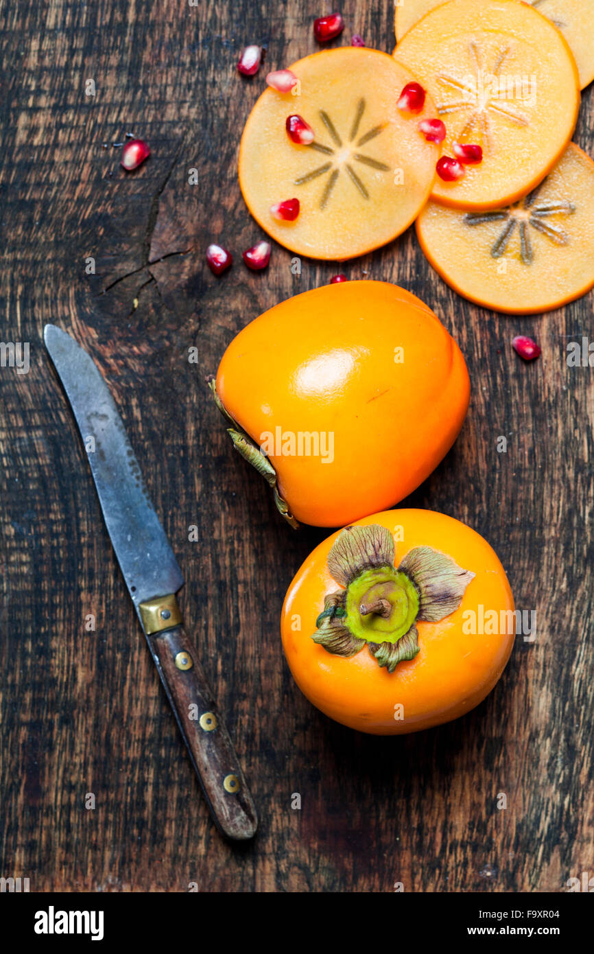 Whole and sliced kaki, knife and pomegranate seed on dark wood Stock Photo