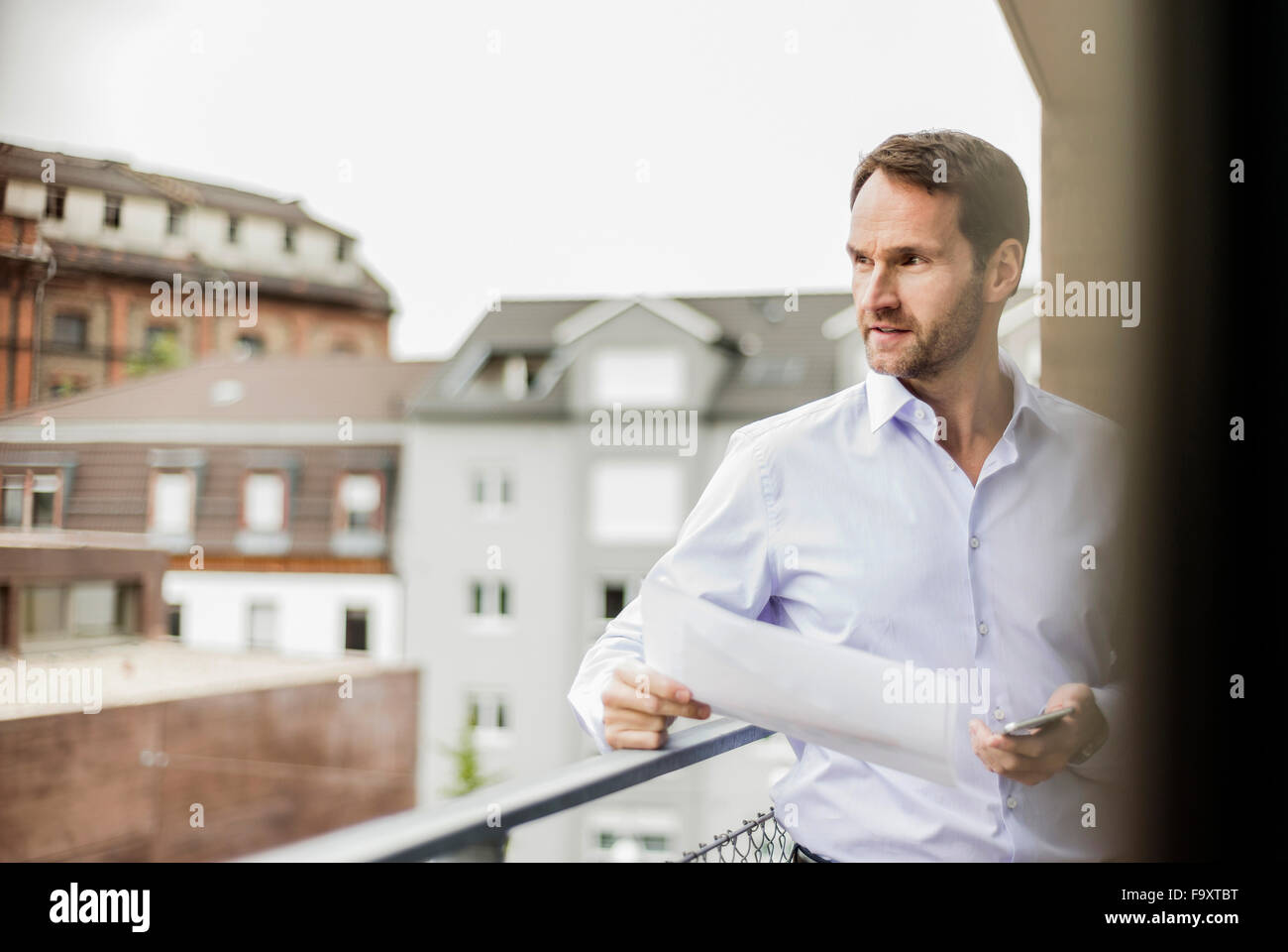 Portrait of businessman with sheet of paper and smartphone looking at distance Stock Photo
