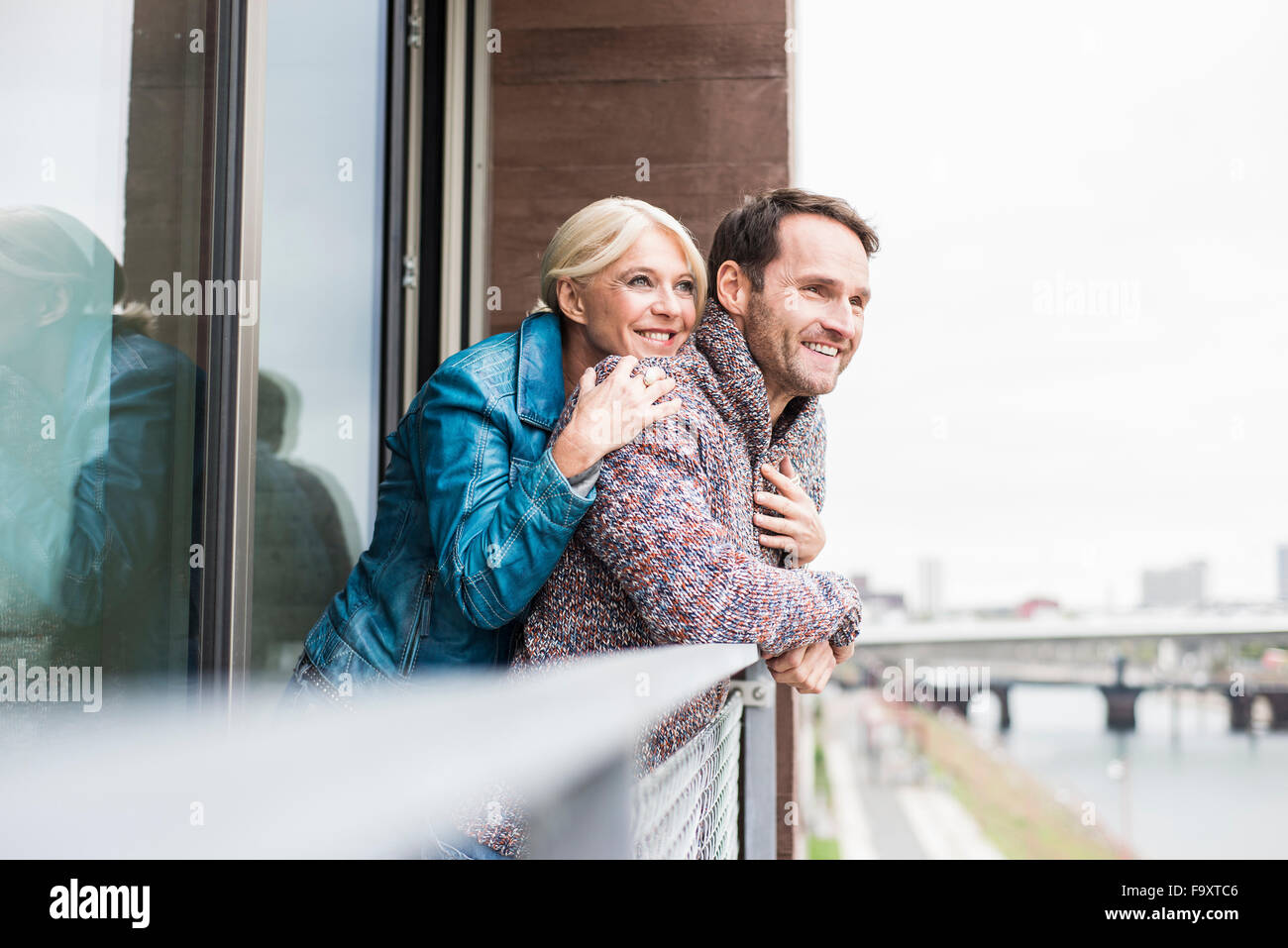 Happy couple standing together on balcony looking at distance Stock Photo