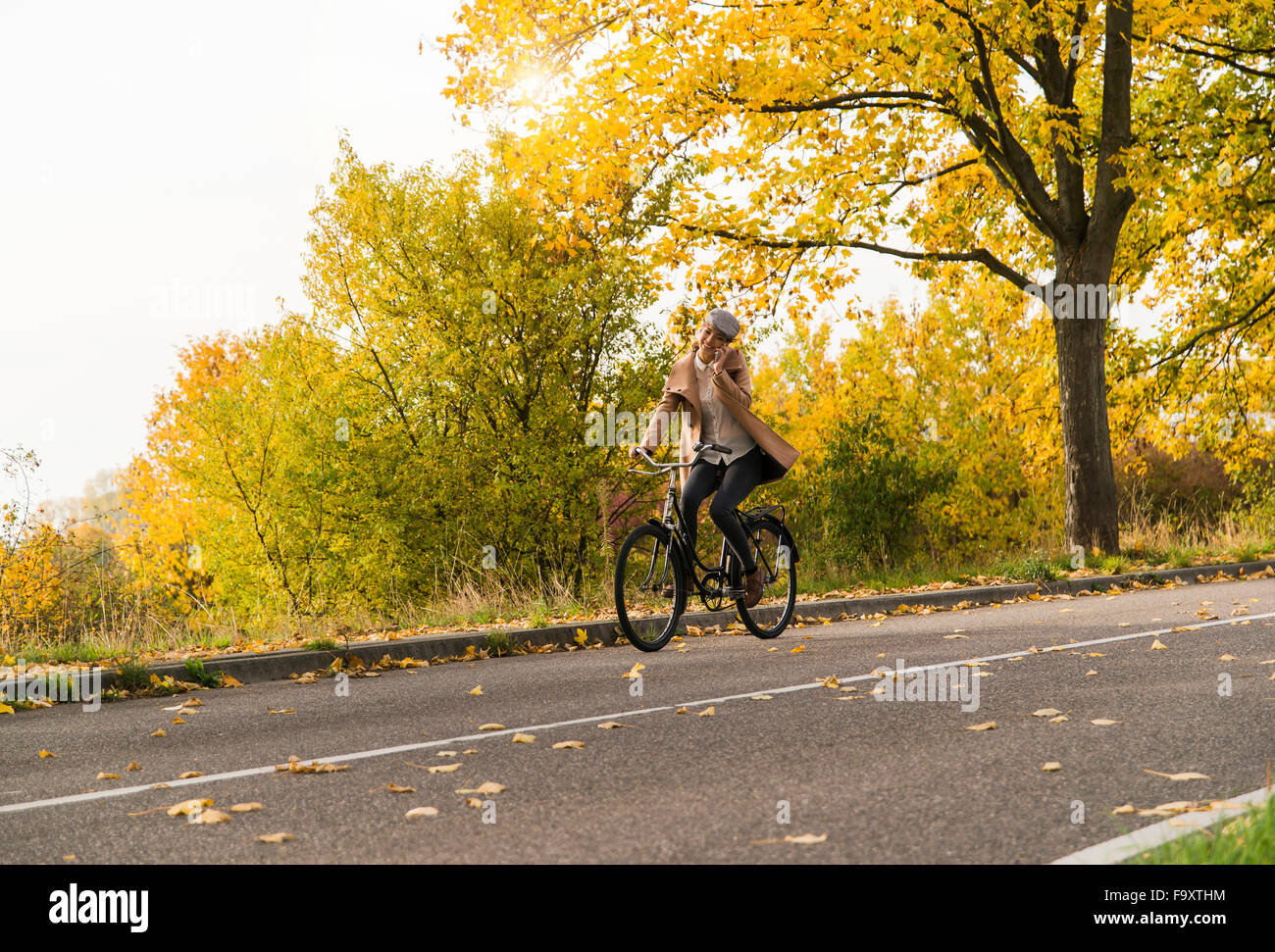 Young woman on cell phone riding bicycle in autumn landscape Stock Photo