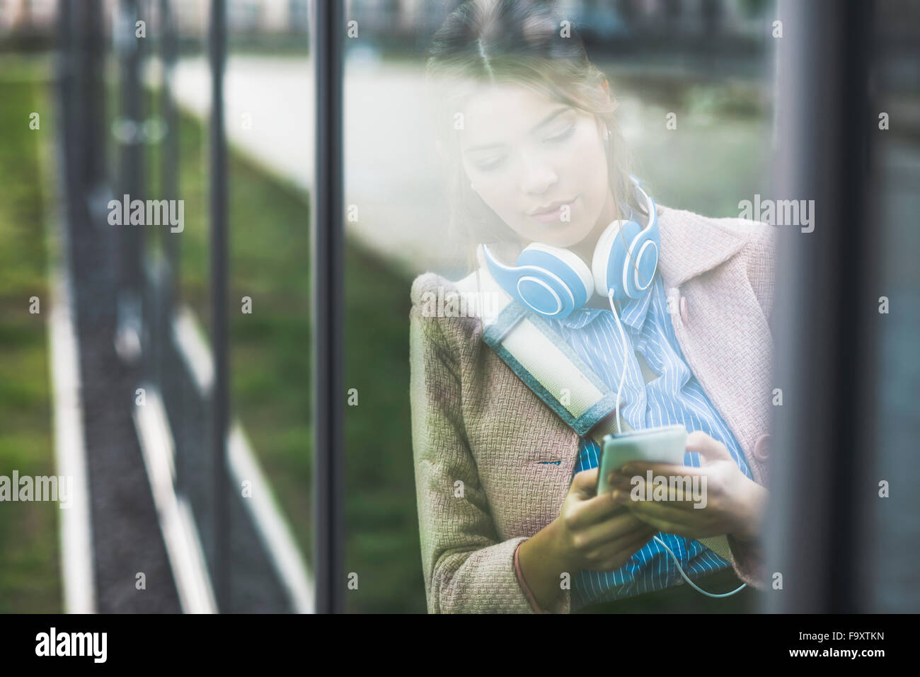 Young woman leaning at glass front looking on cell phone Stock Photo