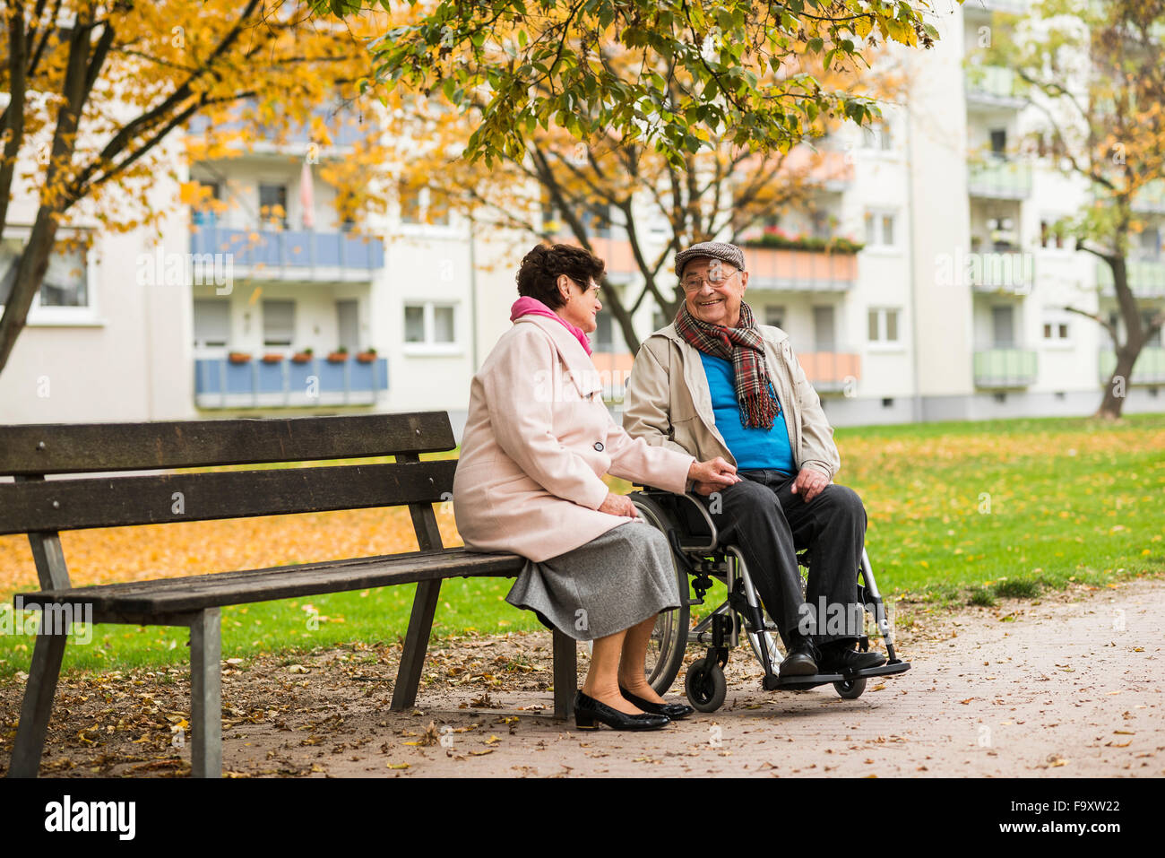 Senior woman sitting on bench next to husband in wheelchair Stock Photo