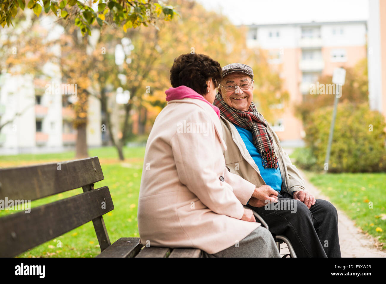Senior man in wheelchair holding hands with wife on bench Stock Photo
