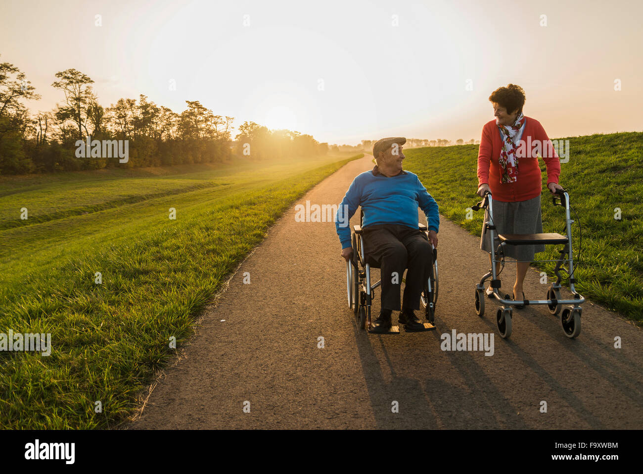 Smiling senior couple with wheelchair and wheeled walker on a path Stock Photo