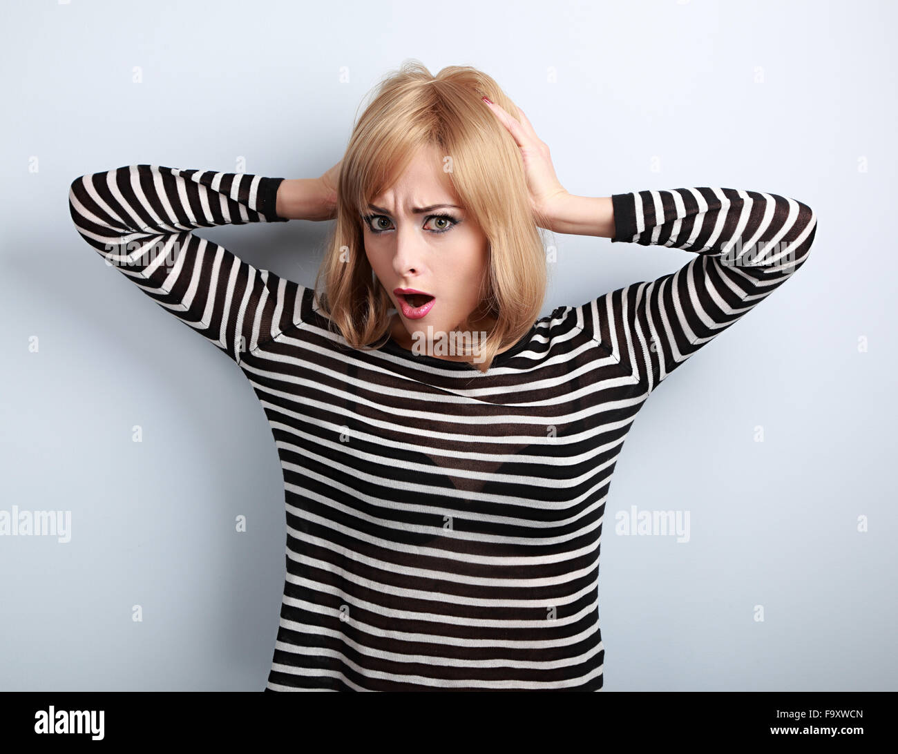 Confused young woman with surprising big eyes holding hand hair. Stress