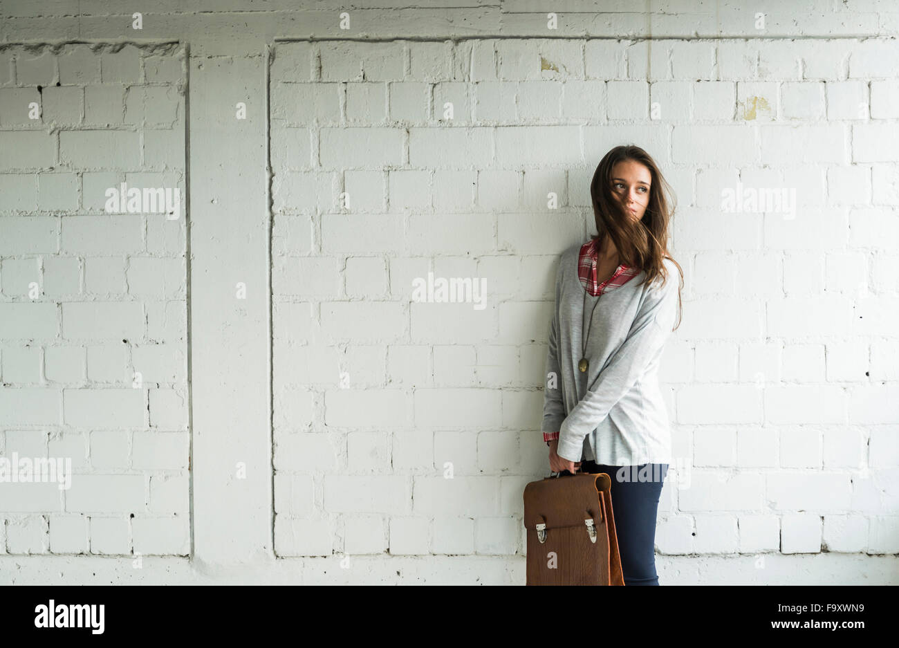 Young woman at brick wall holding satchel bag Stock Photo