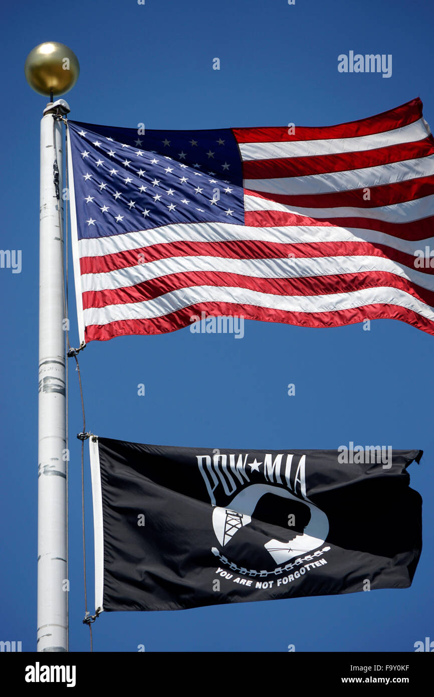 The flag of United States flying over a Prisoner Of War / MIssing in Action flag on a flag pole against blue sky Stock Photo