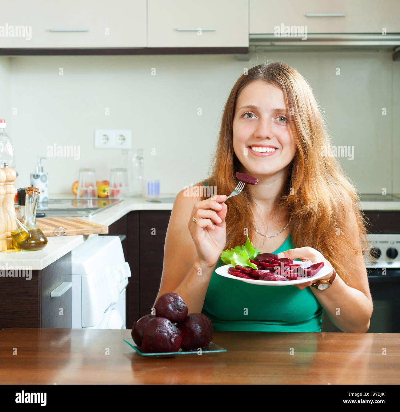 Cheerful ordinary girl eating boiled beets at home interior Stock Photo