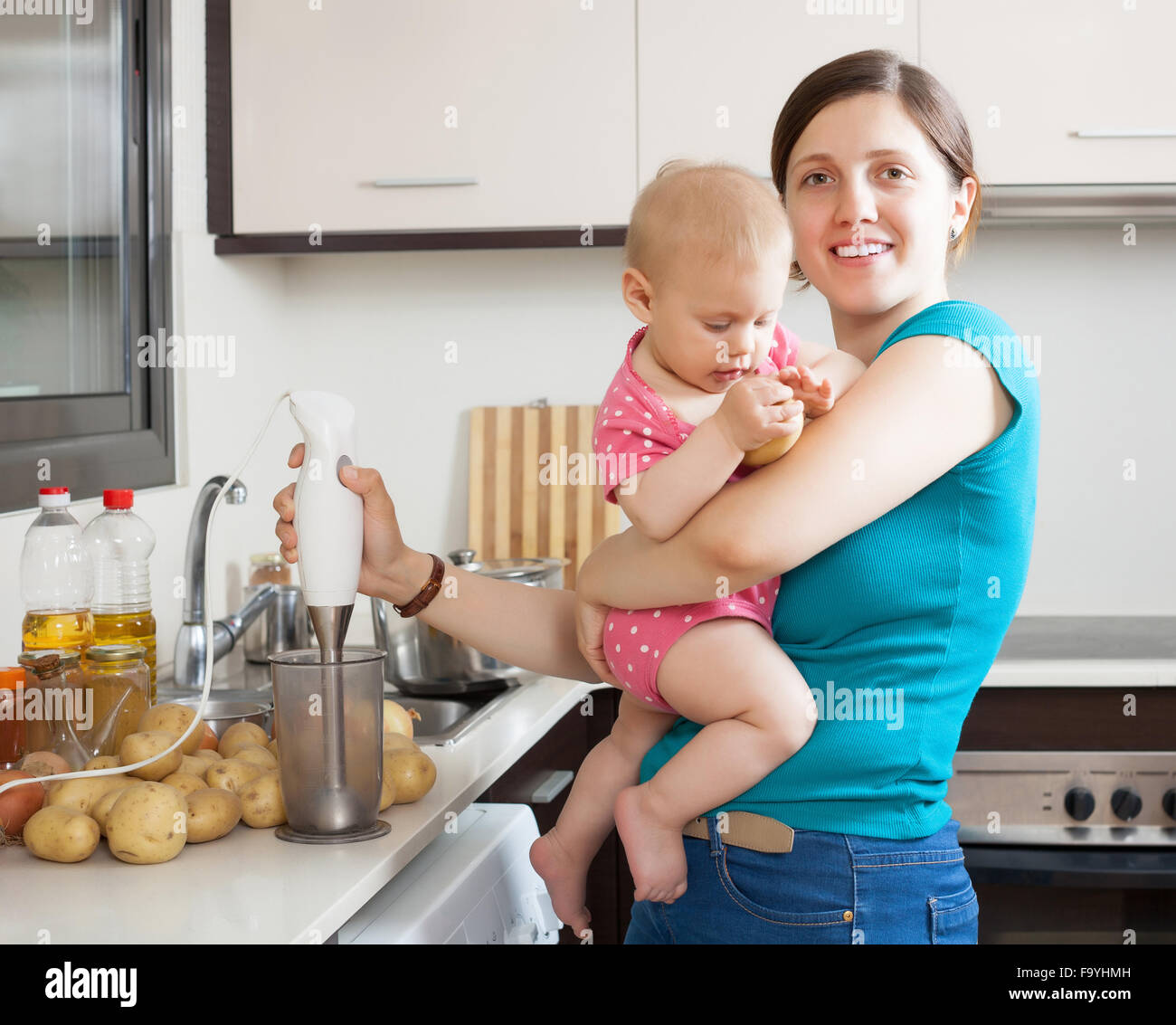 Happy mother and child cooking mashed potatoes with blender in kitchen at home Stock Photo