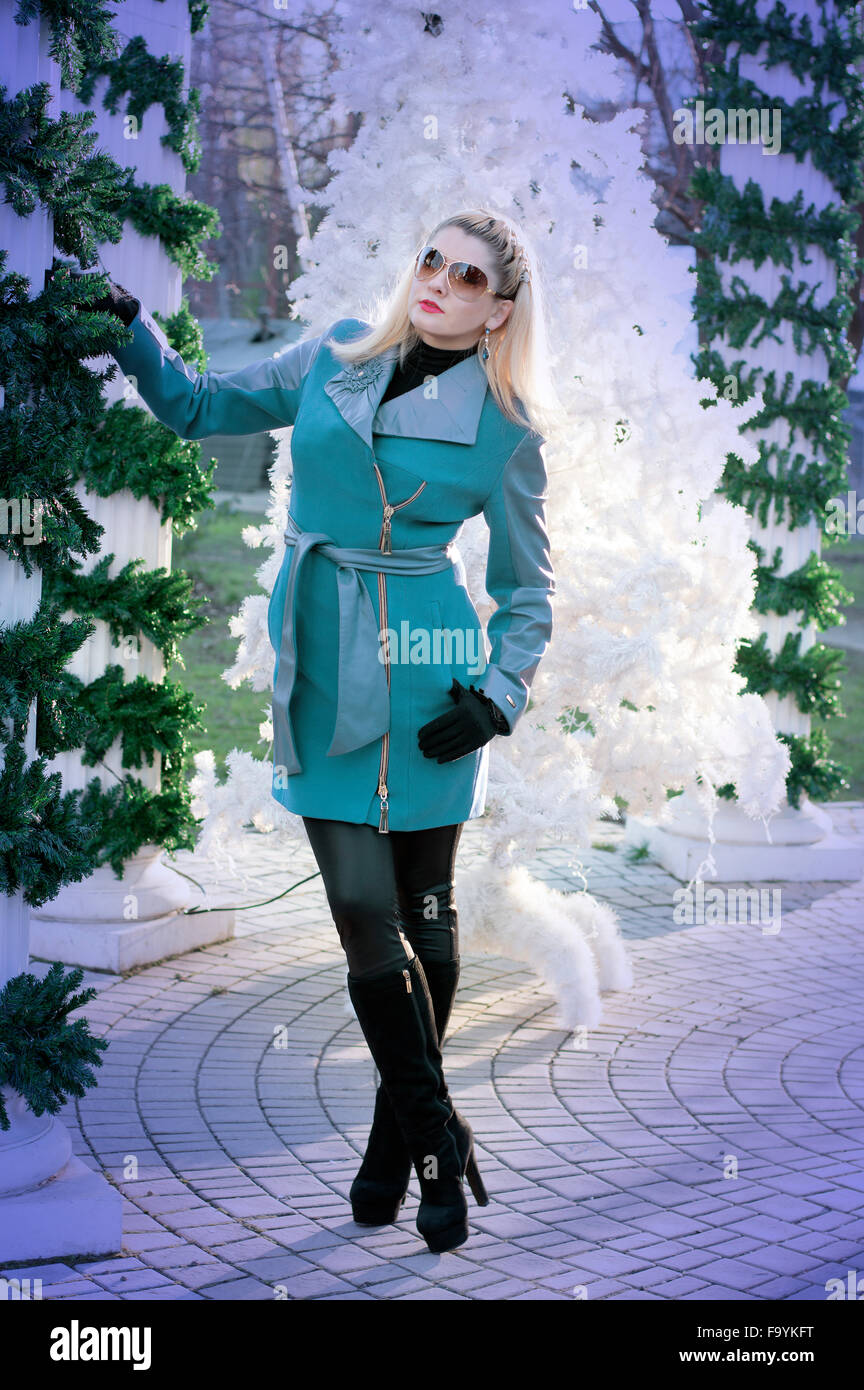 the beautiful woman in a turquoise coat at the columns braided by fir-tree branches, a subject the woman and holidays Christmas Stock Photo