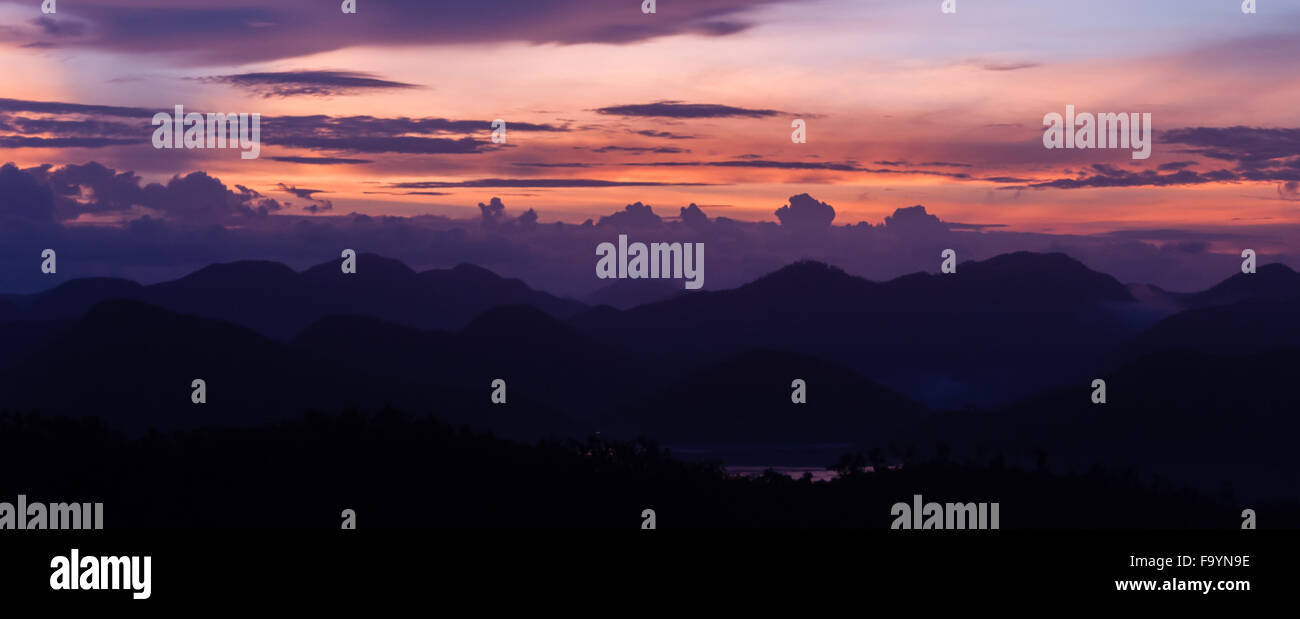 Silhouette of Mountains Above the Water under purple cloudscape clouds at sunset Stock Photo