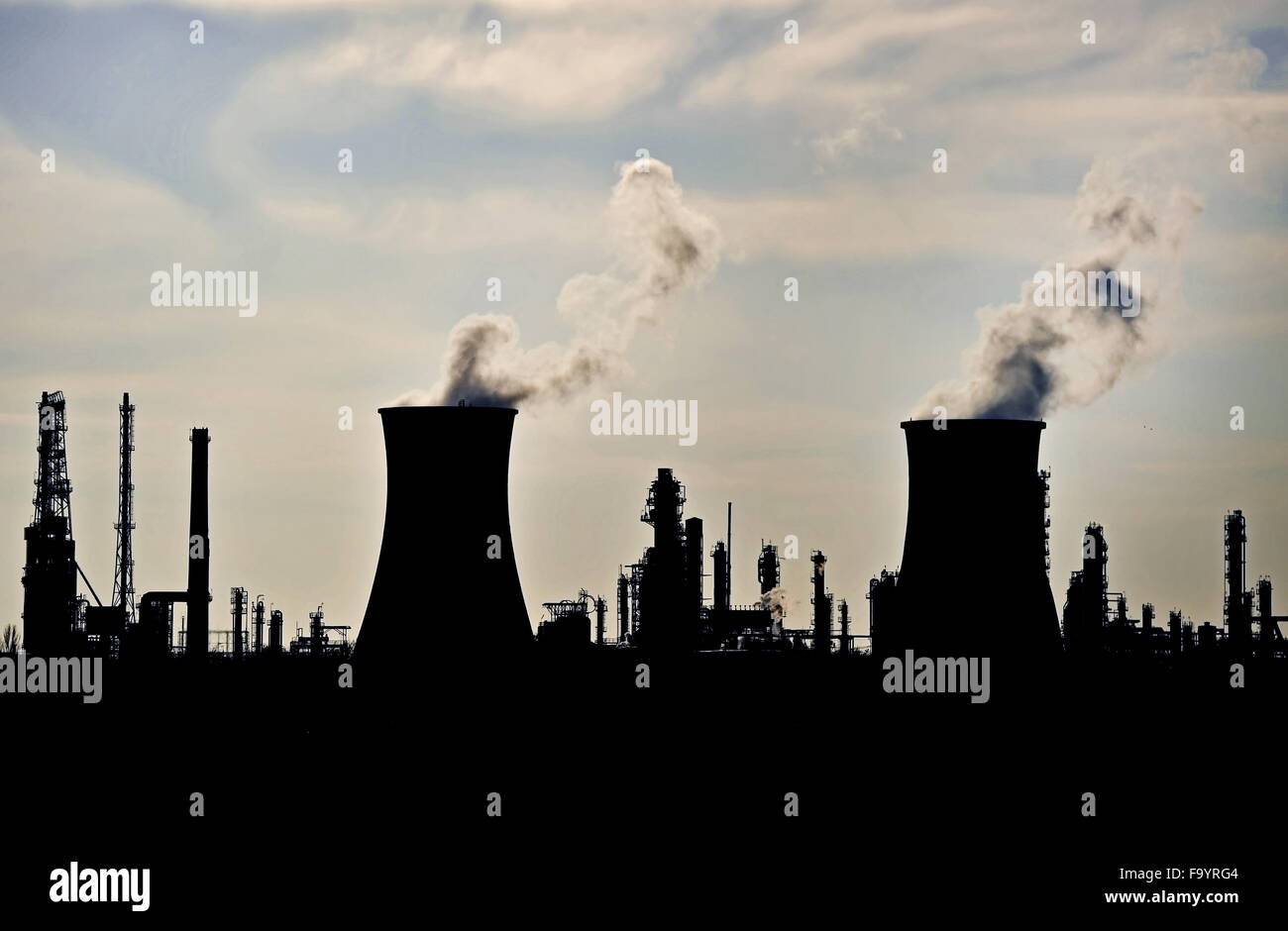 Smoke and steam coming out from industrial petrochemical plant chimneys silhouetted against the sky Stock Photo