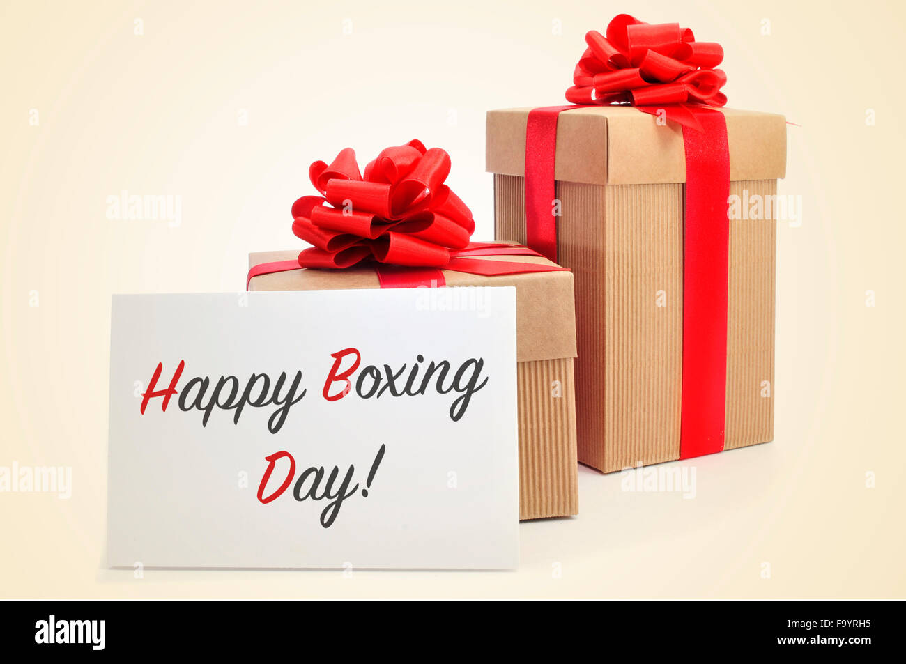 some gifts tied with red ribbon and a signboard with the text happy boxing day, on a beige background Stock Photo