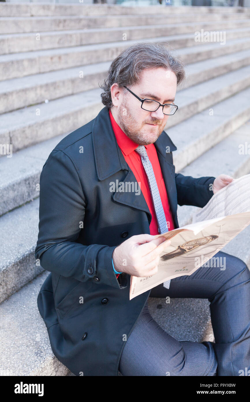 A young businessman with glasses reading a newspaper is thinking in ...