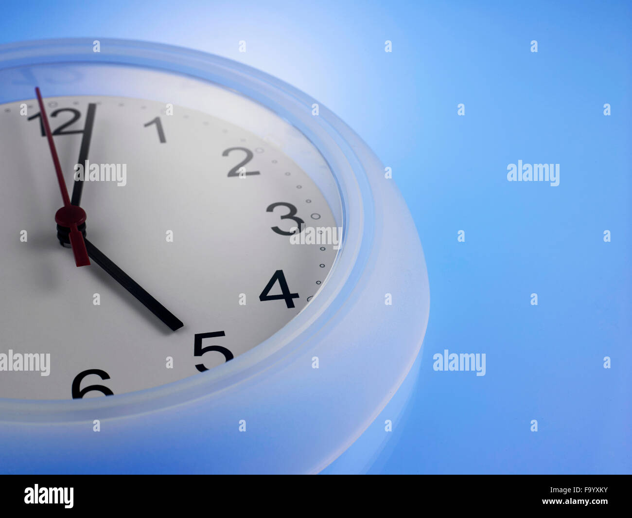 Close up of Clock showing 5 o'clock on a blue wall Stock Photo