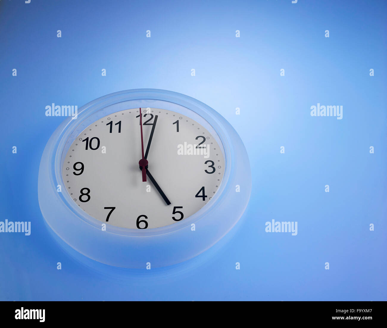 Clock showing 5 o'clock on a blue wall Stock Photo Alamy