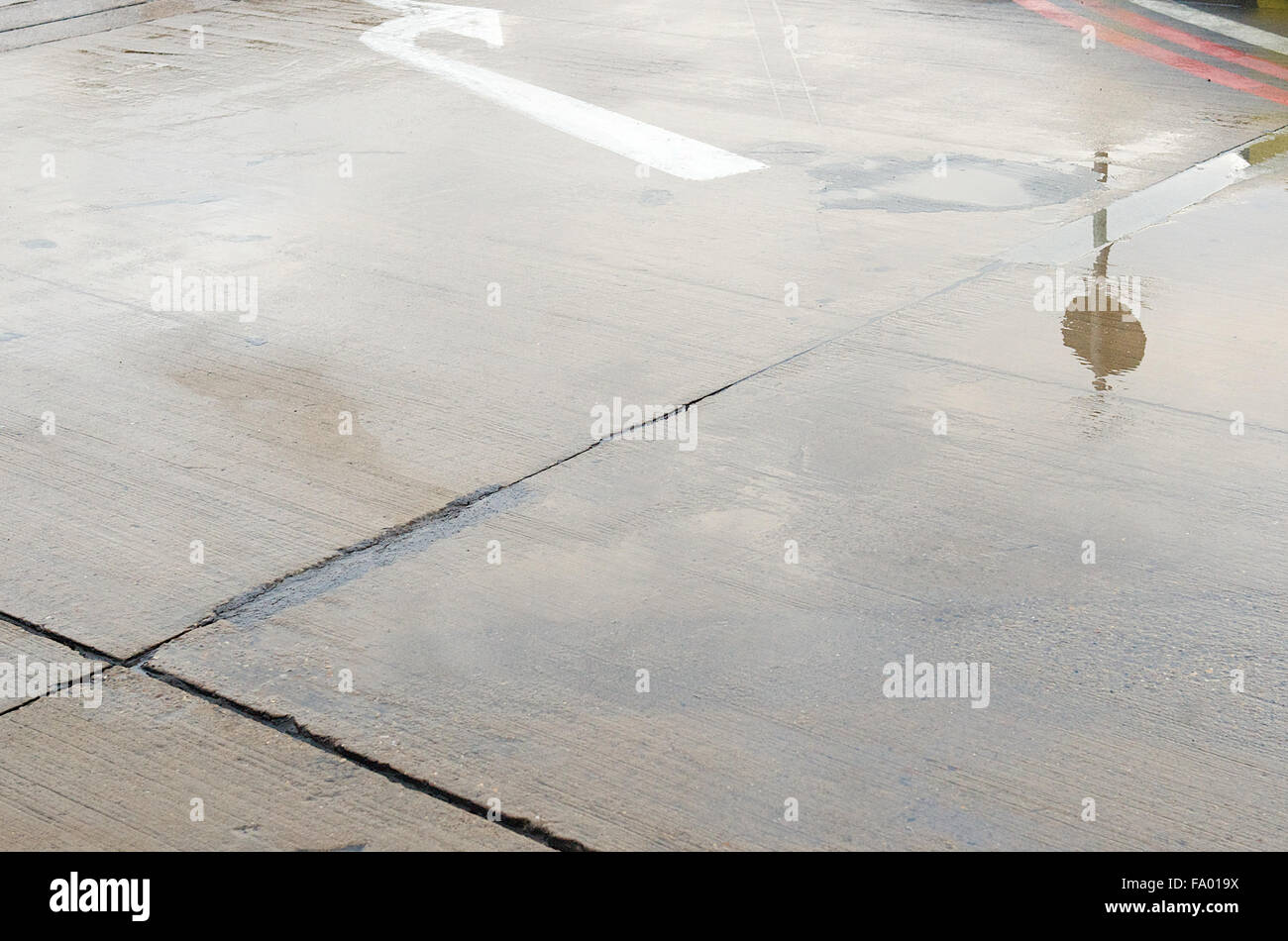 A wet concrete pavement with a white sign on it at Heathrow airport