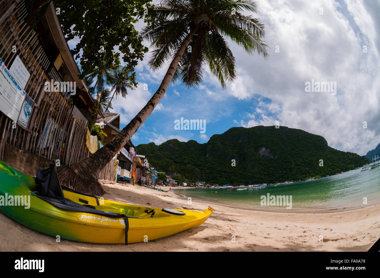 Yellow kayak laying on the sand beach with palm tree Stock Photo