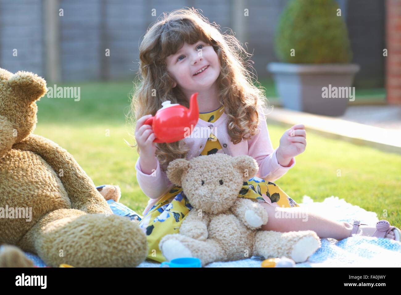 Girl having teddy bear picnic in garden holding toy teapot Stock Photo