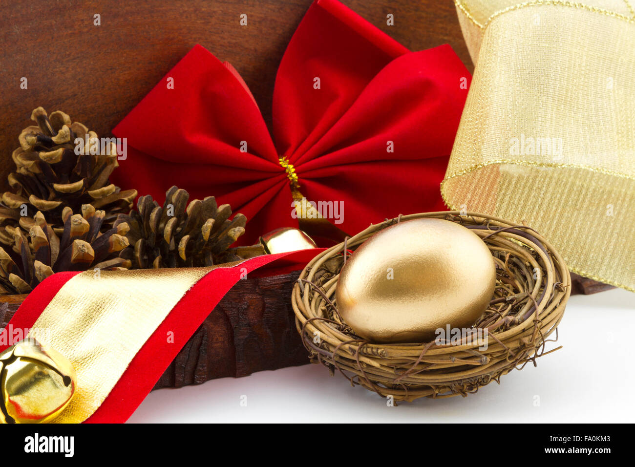 Gold egg in twig nest with holiday red bow and pine cones in wood box offers a rustic, home style view of financial savings Stock Photo