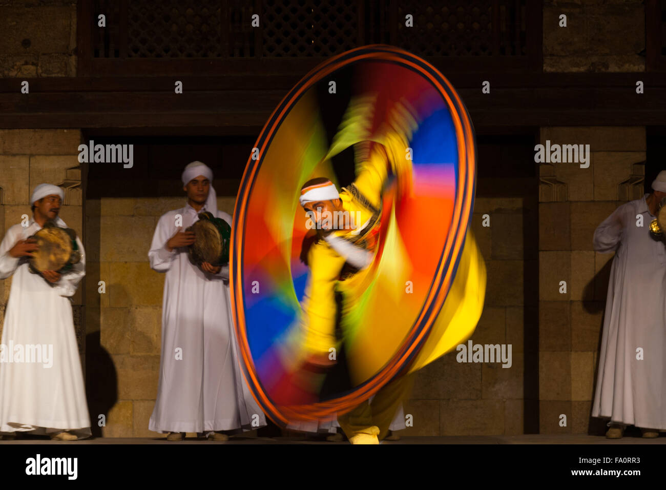 Male Egyptian Sufi dancer in yellow spinning a colorful circular sheet during whirling dervish at open air courtyard performance Stock Photo