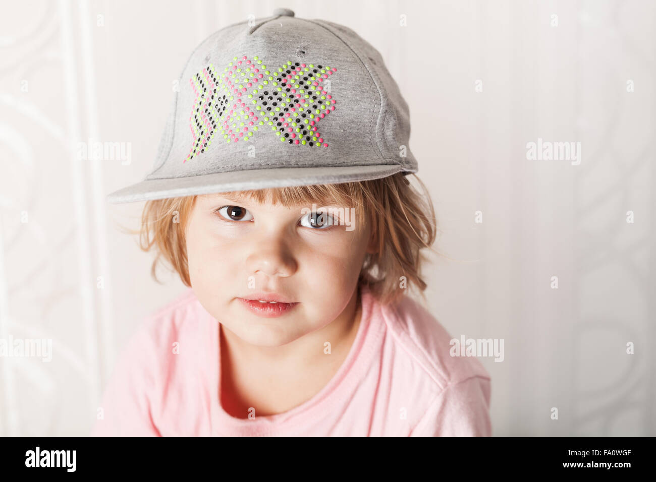 Closeup portrait of cute Caucasian blond baby girl in pink t-shirt and gray cap Stock Photo
