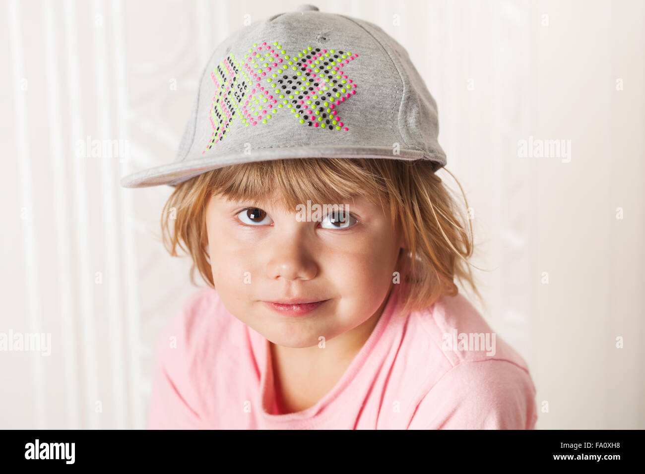 Closeup portrait of cute confused Caucasian blond baby girl in gray cap Stock Photo