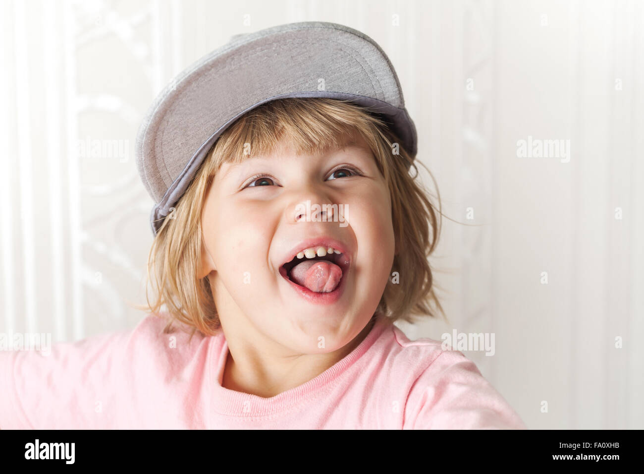 Closeup portrait of funny laughing cute Caucasian blond baby girl in gray cap Stock Photo