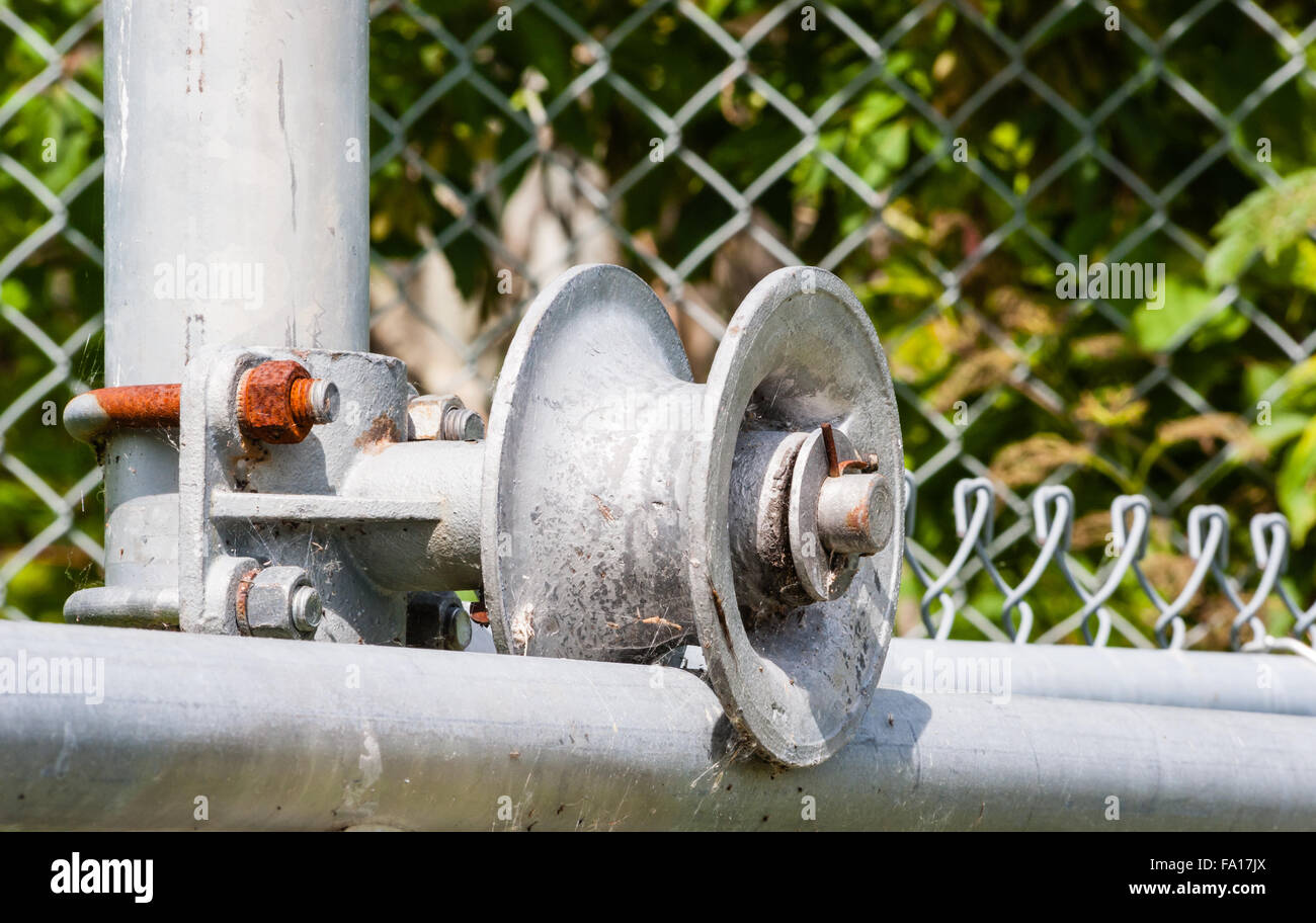 Dirty worn metal roller on frame of chainlink fence gate with rusted screw and nut Stock Photo