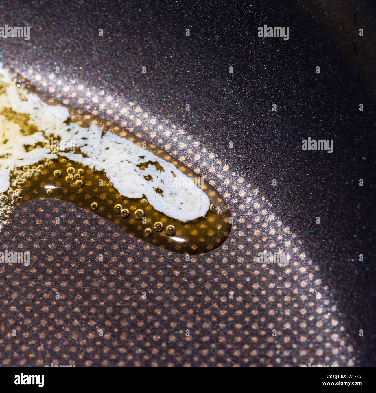 Macro close-up of butter with bubbles slowly melting along curve in black Teflon frying pan. Stock Photo