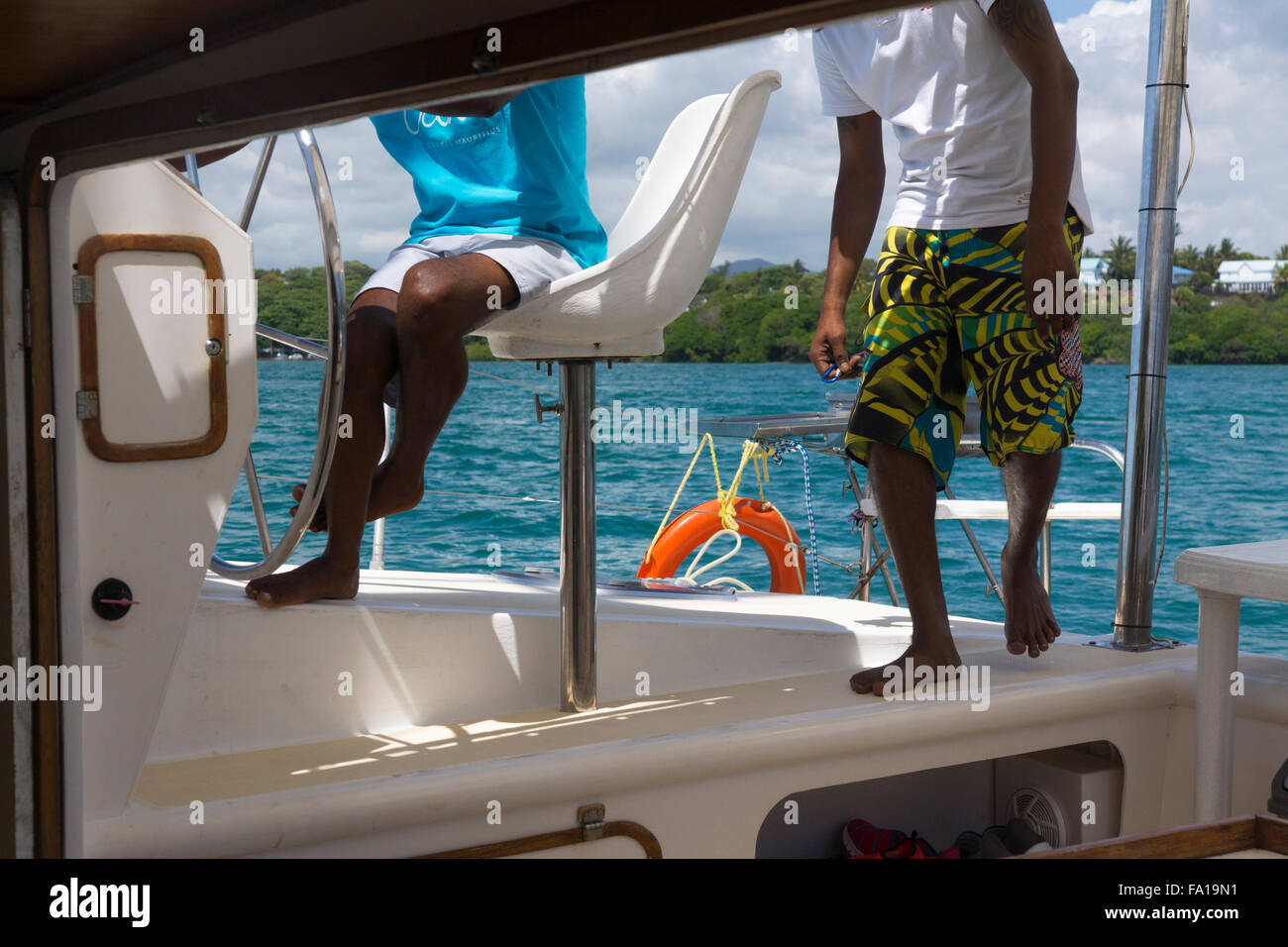 A mauritian steersman steering a catamaran with tourists off the Mauritian coastline Stock Photo