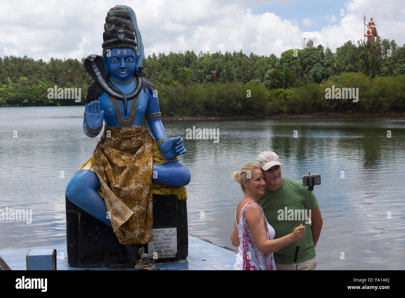 A couple taking a selfie using a selfie stick in front of the Hindu god Shiva at Ganga Talao - Hindu pilgrimage site Stock Photo