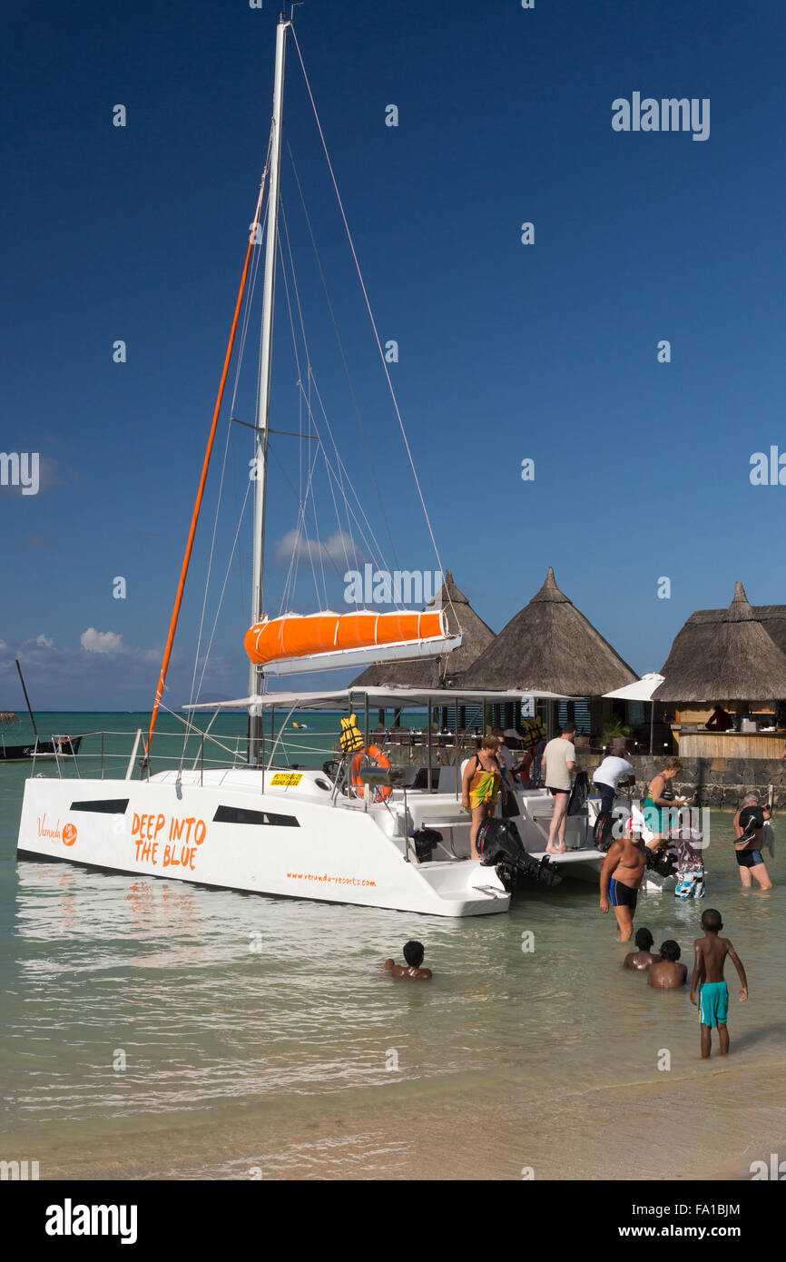 Tourists disembarking from a catamaran, watched by local children in Mauritius Stock Photo