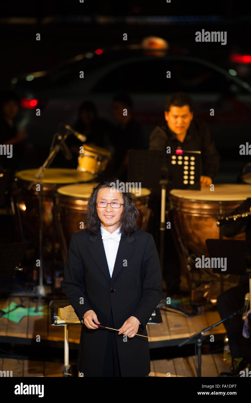 A long haired unidentified conductor of a symphony orchestra accepts applause in the spotlight at a free summer night concert Stock Photo