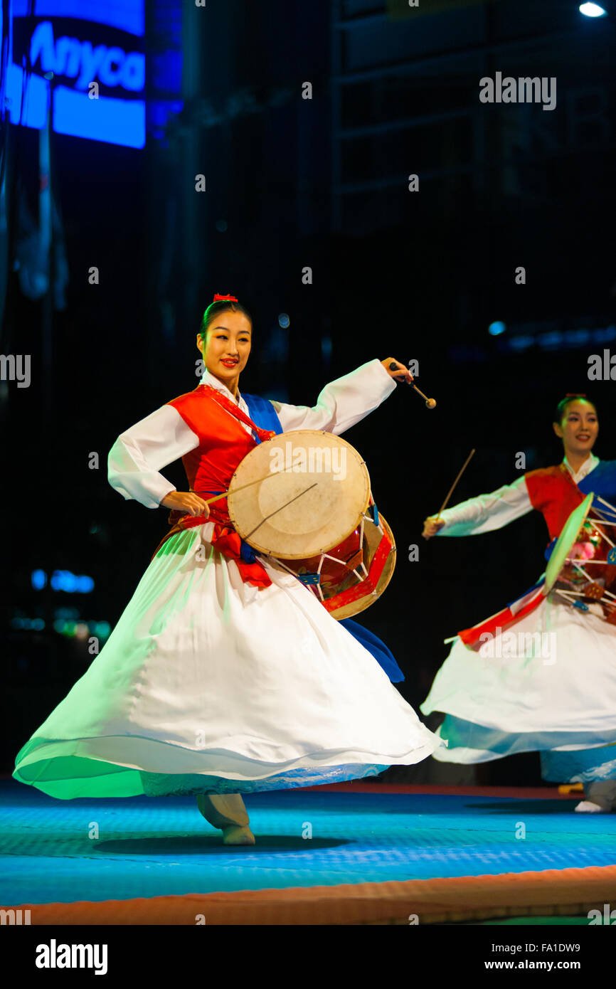 A Korean women in white fluttering hanbok spinning, twirling and playing traditional janggu