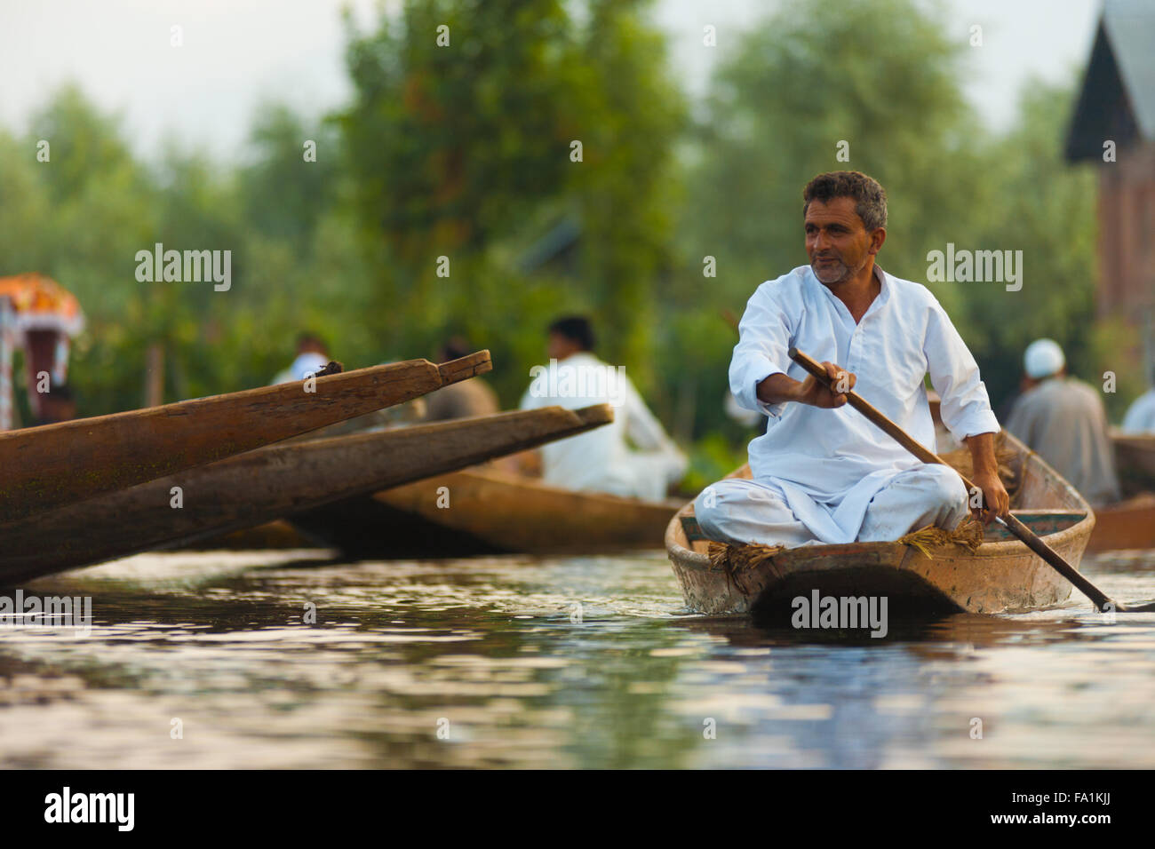 Kashmiri man rowing shikara boat past what remains of the morning floating market on Dal Lake in Kashmir Stock Photo