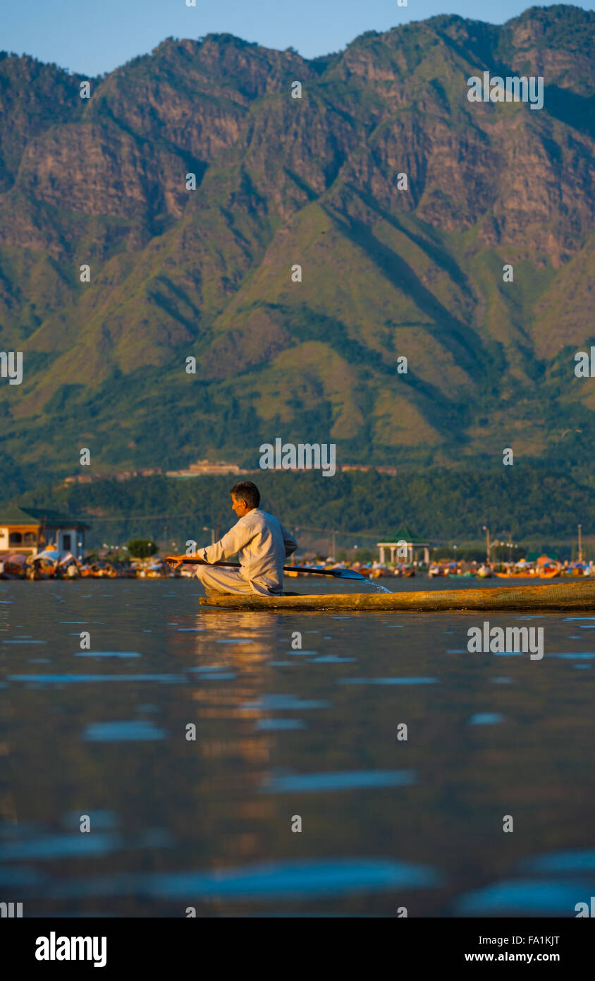 Kashmiri Muslim man rows his boat on the tourist destination of Dal Lake, surrounded by mountains in Kashmir Stock Photo