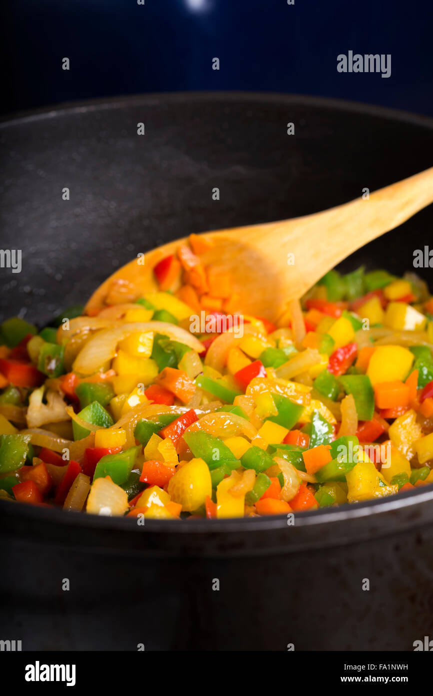 Bell peppers (pepperoni) pan-fried with carrot and onion wooden spoon Stock Photo