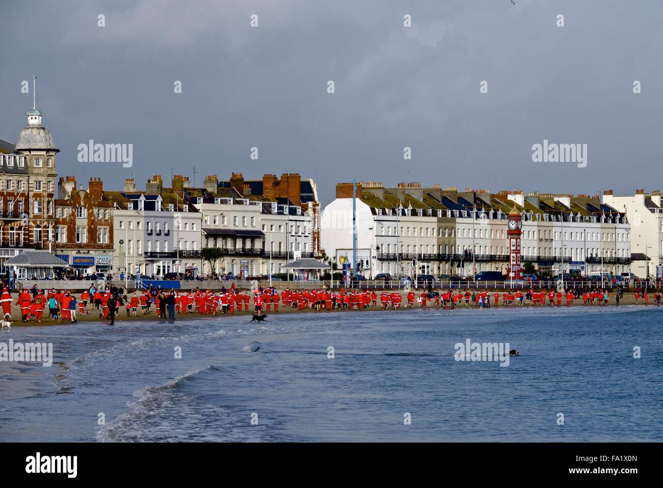 Weymouth, Dorset, UK. 20th Dec 2015. Hundreds of Santas race across Weymouth beach in spring like temperatures taking part in the Christmas Pudding race. The 5k annual charity race started when over 200 Santas chased the Weymouth Panto star Nurse Nellie (played by Lee Redwood) along Weymouth's famous beach Credit:  Tom Corban/Alamy Live News Stock Photo