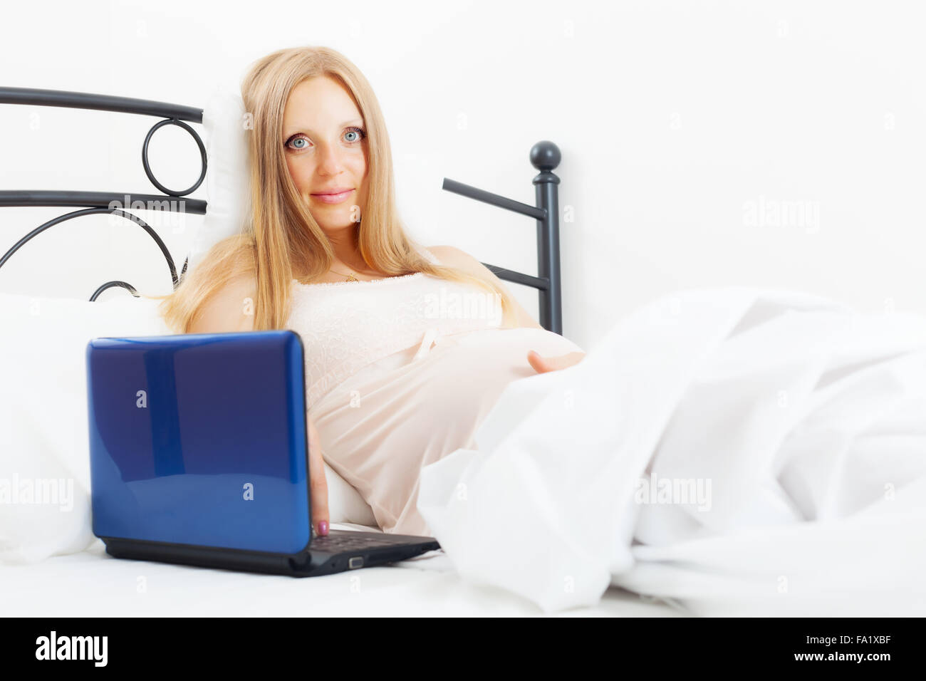 pregnancy woman awaking with laptop on white sheet in her bed at home