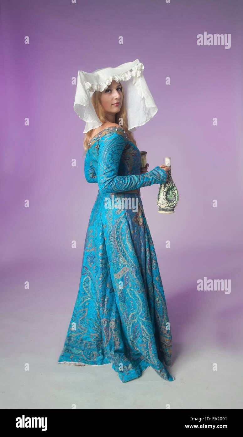 Studio shot of beautiful girl dressed as a medieval noblewoman standing half-turned on purple background Stock Photo