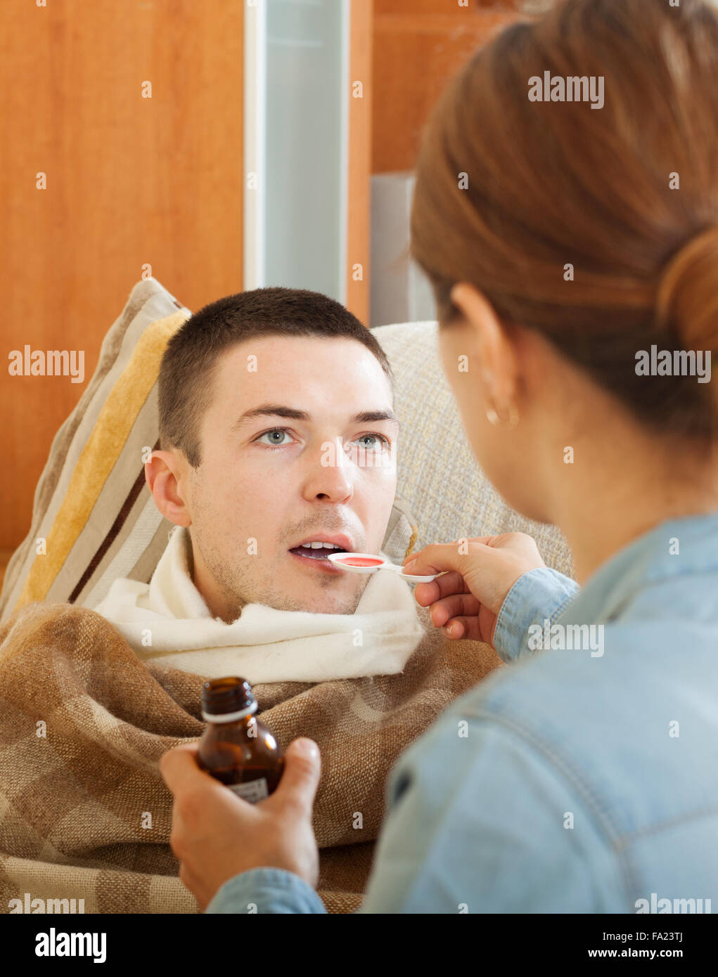 caring woman giving cough syrup to unwell man Stock Photo