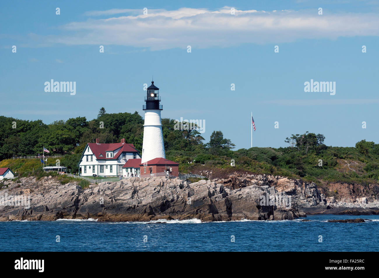 View from water of Portland Head lighthouse which shines brightly to guide mariners around Portland Harbor in Maine on a summer day. Stock Photo