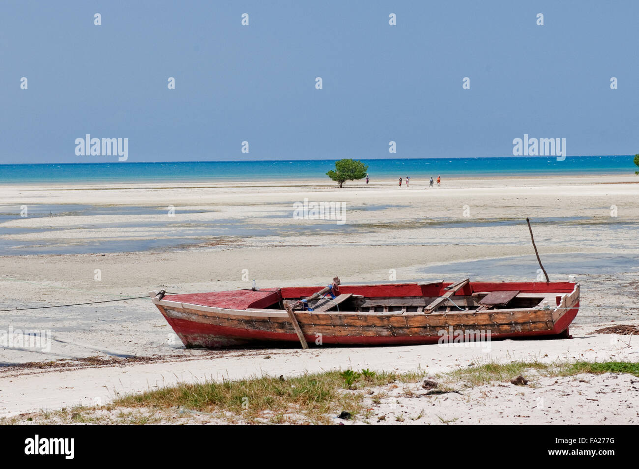 A beach with white sand and blue sky and blue sea with fishermen's boats and some locals in Zanzibar, Tanzania, East Africa Stock Photo