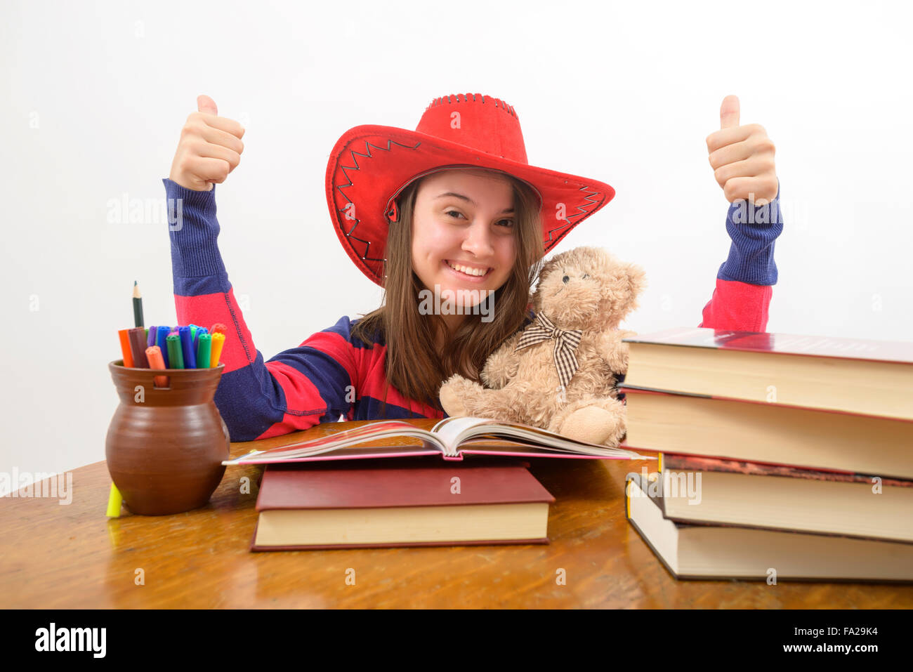 Girl with thumbs up sign sitting on the table with stack of books Stock ...